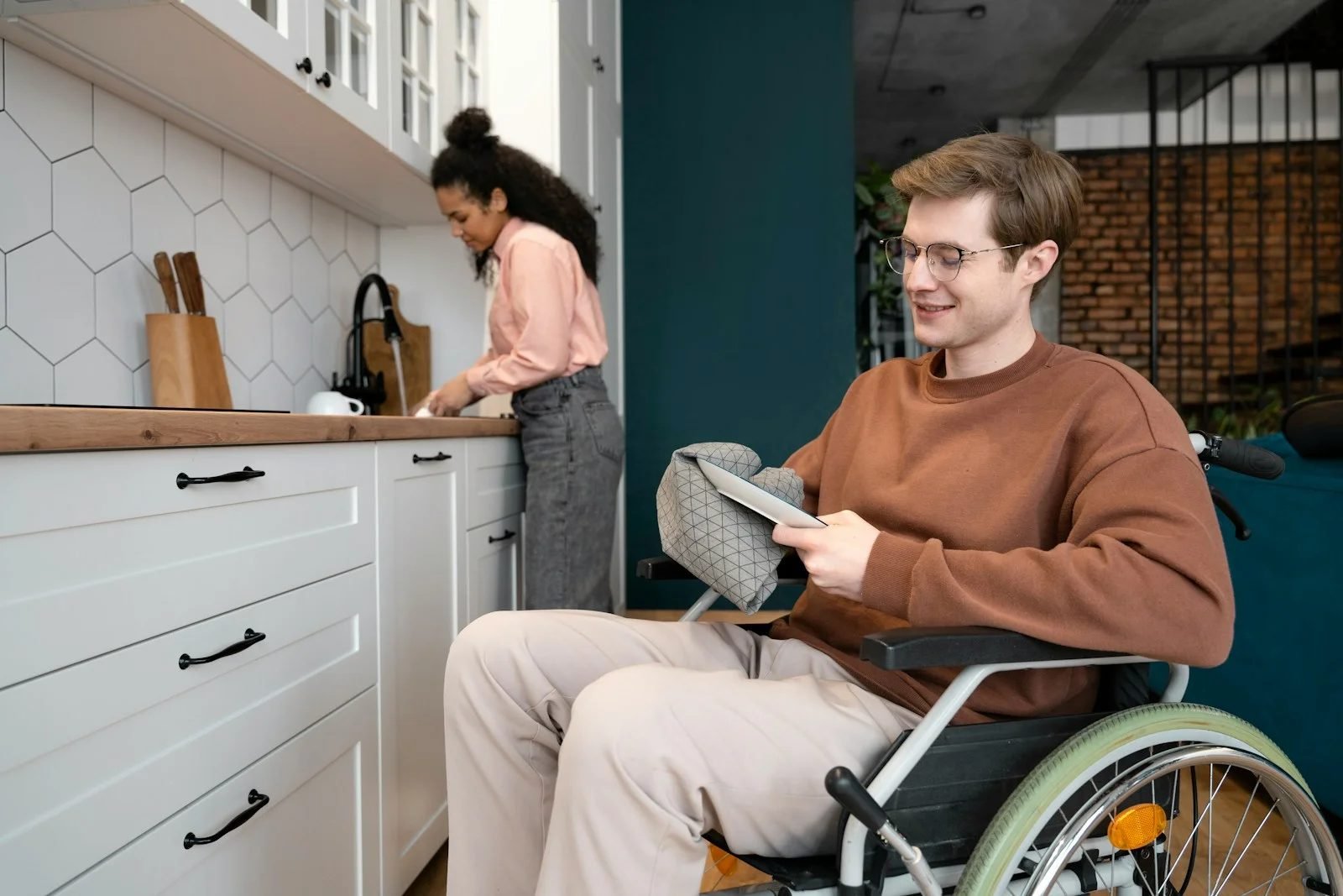 A young man in a wheelchair in his kitchen at home, with his support worker